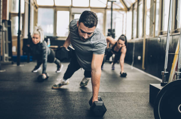 Two young fitness women exercise with dumbbell with personal trainer in the gym Two young fitness women exercise with dumbbell with personal trainer in the gym
